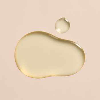 Dwie złociste krople oliwki do skórek OPI Nature Strong na jasnobeżowym tle, widok z góry.