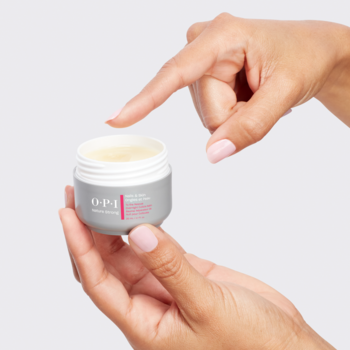 Nocny balsam OPI To The Rescue w szarym słoiczku, aplikowany palcem na skórki, widoczna gęsta, żółtawa konsystencja.