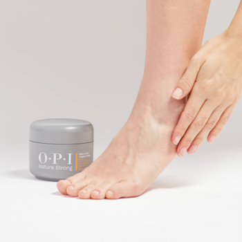 Słoiczek OPI Nature Strong peelingu do stóp i rąk obok kobiecej stopy z dłonią delikatnie masującą piętę.