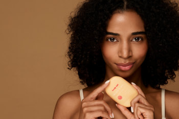 Kobieta trzyma żółty krem do rąk Handy Lab. Glow & Go Silky Touch, odżywczy i regenerujący, na beżowym tle.