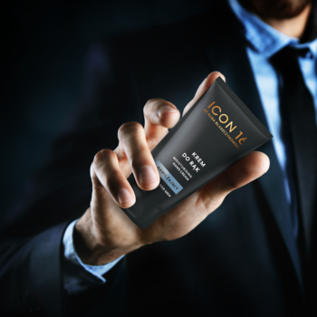 Męska dłoń w garniturze trzyma czarną tubkę nawilżającego kremu do rąk ICON 14. Widok pod kątem.