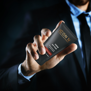 Dłoń w garniturze trzyma czarny krem do rąk ICON 16. Etykieta z nazwą produktu widoczna, idealny do suchej skóry.