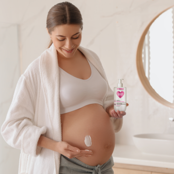 Ciężarna kobieta w szlafroku aplikuje naturalny ujędrniający balsam do ciała na brzuch, trzymając butelkę.