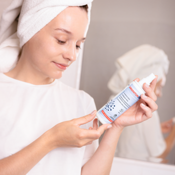 Kobieta w ręczniku trzyma aerozol Srebro Argentum200 z cytrynianem srebra do cery trądzikowej, widok z bliska.