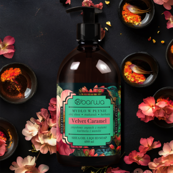 Mydło w płynie Barwa Velvet Caramel w brązowej butelce z pompką na ciemnym tle z kwiatami i miseczkami.