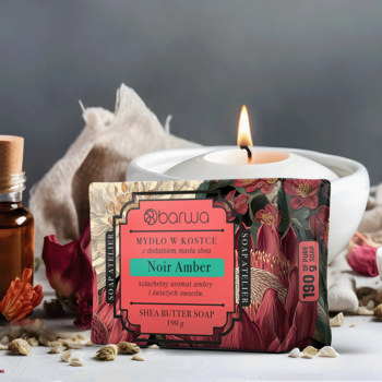 Barwa Noir Amber mydło shea w ozdobnym opakowaniu z kwiatami na tle świecy i olejków, widok z przodu.