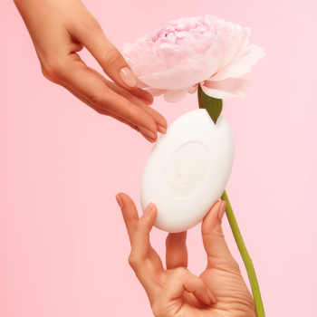 Pani Walewska SOFT & GLOW mydło w białej, owalnej kostce, delikatnie trzymane z różowym kwiatem na pastelowym tle.