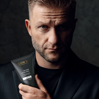 Mężczyzna z zarostem i intensywnym spojrzeniem trzyma kojący balsam po goleniu CON 11 w ciemnej tubce.