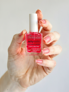 Ręka trzyma butelkę różowego lakieru Bielenda Jelly Nails Cherry Jelly Pop 2w1 z efektem gloss. Pomalowane paznokcie.
