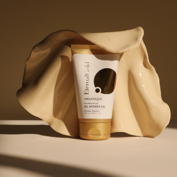 Eternal Gold żel-olejek do mycia w kremowej tubce na beżowej fali, z czarnym logo.