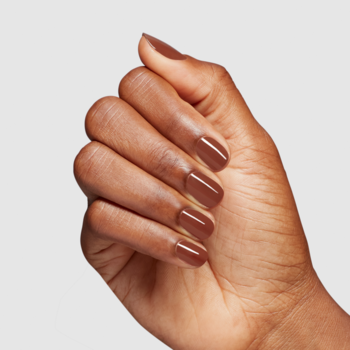 Dłoń o ciemnej karnacji z brązowym, błyszczącym lakierem do paznokci. Manicure w odcieniu brązu na gładkim tle.