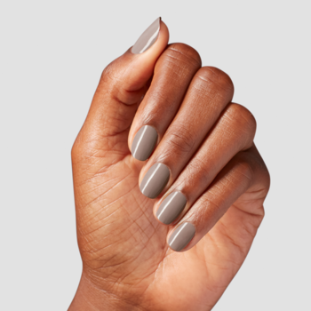 Zbliżenie na dłoń z beżowo-szarym lakierem do paznokci o kremowym wykończeniu, paznokcie wypielęgnowane.