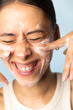 Kobieta z uśmiechem wciera w twarz pianę LUMENE NORDIC - C [VALO] Żel myjący do twarzy o działaniu złuszczającym.