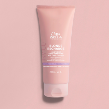 Odżywka Wella Invigo Blonde Recharge w różowej tubce z fioletowym paskiem na pastelowym tle, widok z przodu.