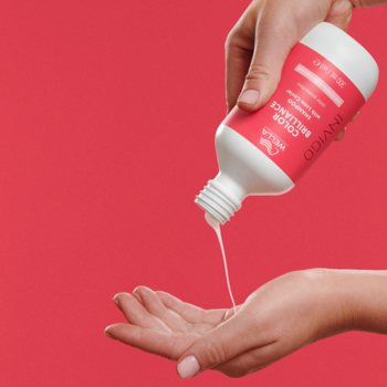 Szampon Wella Invigo Color Brilliance chroniący kolor, wylewany z białej butelki do dłoni na czerwonym tle.
