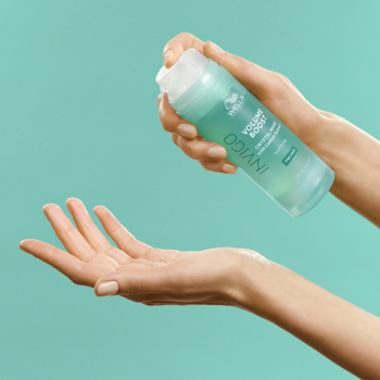 Wella Invigo Volume Boost, maska dodająca objętość. Dłonie aplikują niebieski spray z przezroczystej butelki.