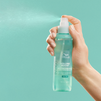 Dłoń trzyma lekki spray Wella Invigo Volume Boost w niebieskiej butelce, rozpylając mgiełkę do objętości włosów.