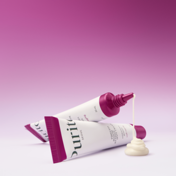 Dwie białe tubki PURITO SEOUL Timeless Bloom Retinol Spot Cream z fioletowymi nakrętkami, krem wyciśnięty na różowym tle.