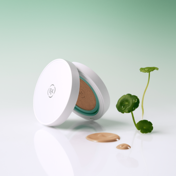 Otwarty krem BB w białym kompakcie, obok krople podkładu i zielone listki wąkroty. Półmatowy efekt.