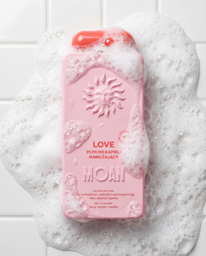 MOAN Płyn do kąpieli Love, różowa butelka z wytłoczonym słońcem, zanurzona w pianie, na białych kaflach.