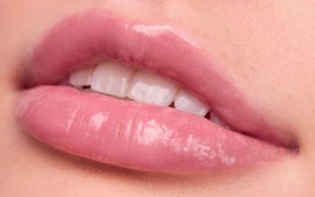 Zbliżenie na błyszczące, pełne usta pokryte różowym balsamem do ust z żelowym wykończeniem, ukazujące białe zęby.