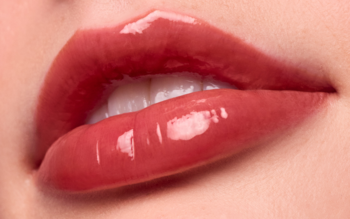 Zbliżenie na pełne, błyszczące usta w odcieniu różowego brązu, pokryte nawilżającym balsamem o żelowym wykończeniu.