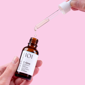 Geek & Gorgeous C-Glow serum 15% wit. C w bursztynowej butelce, kropla spada z pipety. Różowe tło.