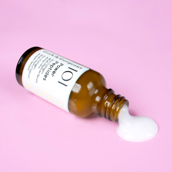 Brązowa butelka serum Power Peptides leży na boku na różowym tle, z białą, kremową zawartością wylaną obok niej.