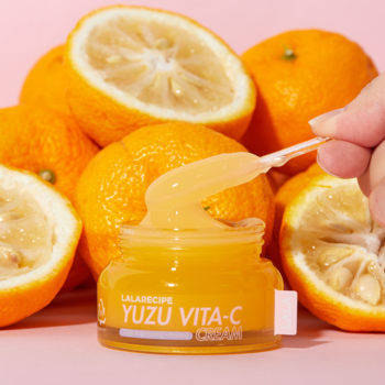 LaLa Recipe Yuzu Vita C Cream, żółty krem w słoiku, ręka ze szpatułką, świeże yuzu, różowe tło.