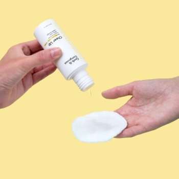 Dłoń wylewa złuszczający płyn Clear Up AHA BHA 6% z białej butelki na wacik; do cery problematycznej. Żółte tło.