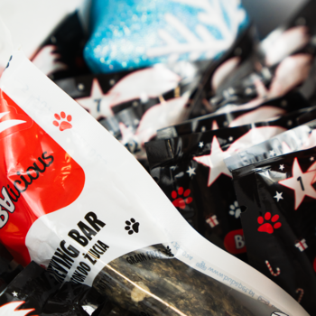 Ujęcie z bliska: naturalny, bezzbożowy baton do gryzienia dla psa w czerwono-białym opakowaniu z łapkami i gwiazdkami.