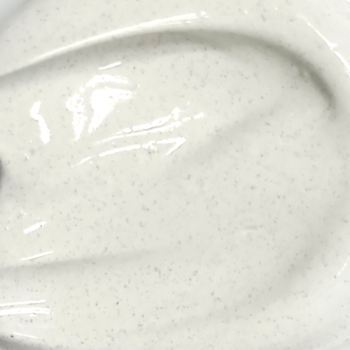 Zbliżenie na kremową teksturę KREM CC MAGIC SKIN, adaptującego się do cery, z widocznymi ciemnymi mikropigmentami.