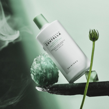 Madagascar Centella Tea-Trica Soothing Sun Milk, biała butelka kremu do twarzy pod kątem, zielone tło z pąkiem.