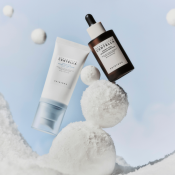 Zestaw Skin1004: biały krem SPF 50 i brązowe serum do twarzy z pipetą, wśród białych kul na błękitnym tle.