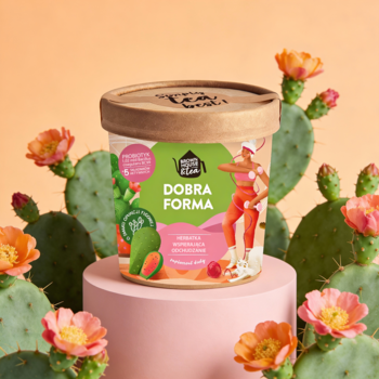 Pojemnik suplementu Dobra Forma, brązowy z zielono-różową etykietą, na różowym postumencie wśród kwitnących kaktusów.