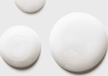 Widok z góry na krople białego, gęstego szamponu zwiększającego objętość z peptydami kolagenowymi na jasnym tle.