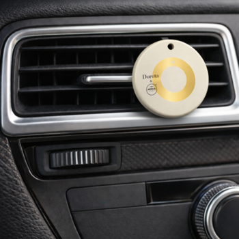 Okrągły odświeżacz powietrza Eleanta beżowo-złoty, wpięty w kratkę nawiewu samochodowego na desce rozdzielczej.