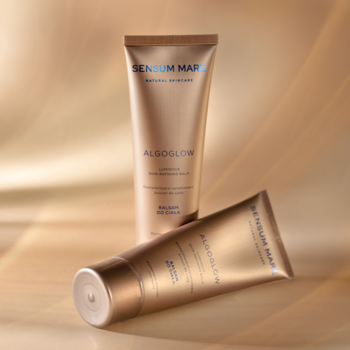 Dwa złote, lśniące balsamy Sensum Mare Algoglow do ciała, jeden stoi, drugi leży, na tle złotego blasku.