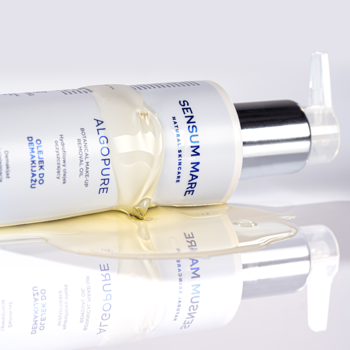 Sensum Mare Algopure hydrofilowy olejek do demakijażu, biała butelka z pompką leży, olejek wylany na lśniące tło.