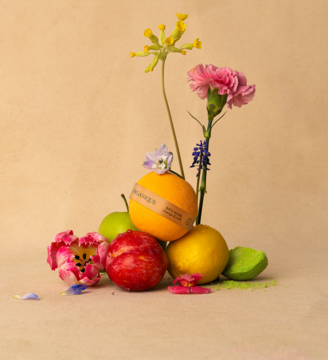 Musująca kula do kąpieli MANGO, z owocami i kwiatami na beżowym tle, widok z przodu. Nawilżająca z olejami.