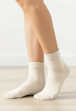 Jasne skarpetki damskie za kostkę, z delikatnym wzorem w skośne paski, noszone na nogach na jasnej podłodze.