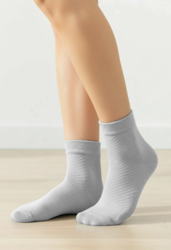 Jasnoszare skarpetki za kostkę z delikatnym, prążkowanym wzorem, noszone na stopach, na tle drewnianej podłogi.
