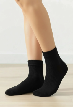 Czarne, krótkie skarpetki damskie z delikatnym rombkowym wzorem, noszone na stopach, na tle jasnej podłogi.