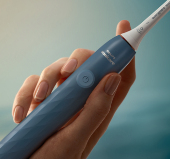 Zbliżenie: niebieska soniczna szczoteczka Philips Sonicare w dłoni, z widocznym przyciskiem zasilania i teksturą.