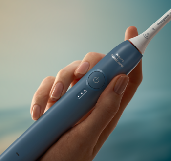 Marine blue Philips Sonicare 3100 sonic toothbrush with white head held in a hand, power button visible.
