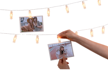 Dłoń wiesza pamiątkową fotografię na girlandzie świetlnej z klipsami, obok widoczne są inne zdjęcia.