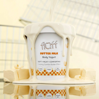 Fluff Butter Milk Body Yogurt, biały kubek z kapiącym kremem, kostki masła na lustrzanym tle, widok z przodu.