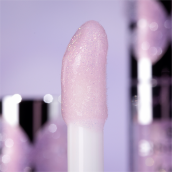 Zbliżenie na biały aplikator błyszczyka z brokatem, jasnofioletowy, mieniący się. W tle fioletowe rozmycie.