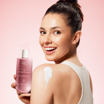 Uśmiechnięta kobieta z różowym regenerującym balsamem do ciała z pompką, z aplikowanym kremem na ramieniu.