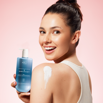 Uśmiechnięta kobieta z naturalnym balsamem do ciała z kwasem hialuronowym. Niebieska butelka, krem na ramieniu.